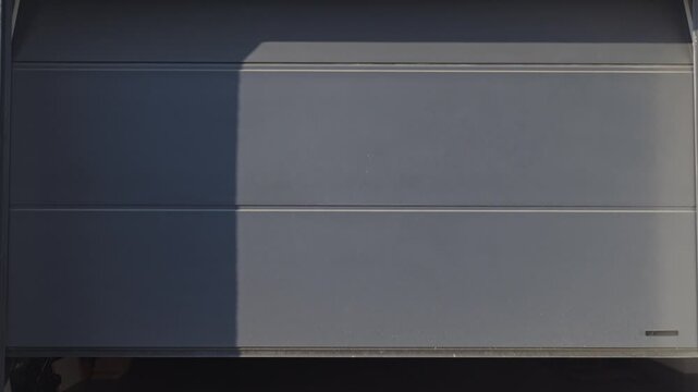 Gray sectional garage door is opening with storage items visible inside. Concept of residential garage access and home storage