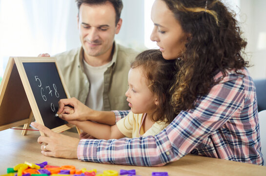 Family parents guide daughter writing numbers and alphabet. At home, child girl learning on a chalkboard as parents guide, making education and homework easier. Supportive education and development.
