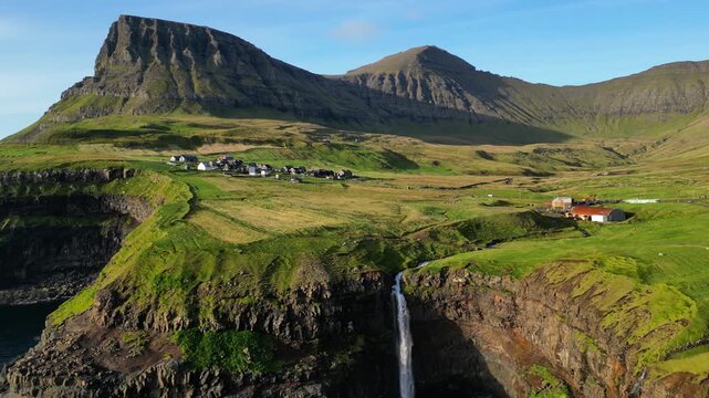 Cinematic 4K aerial drone shot soaring over the rugged cliffs of Gasadalur and Mulafossur waterfall