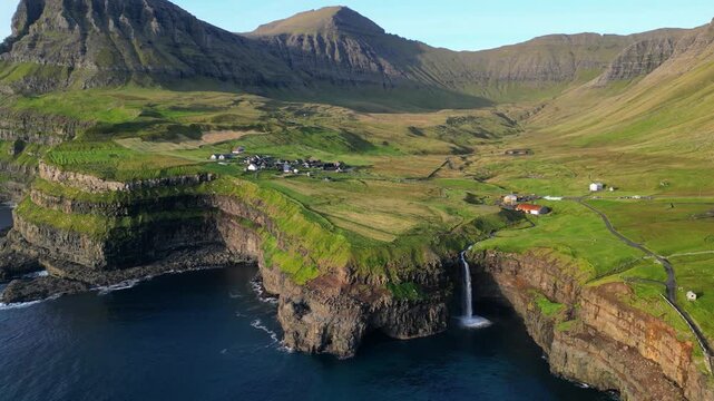 Cinematic 4K aerial drone shot soaring over the rugged cliffs of Gasadalur and Mulafossur waterfall