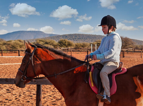 Young Girl Learning to Ride a Bay Horse in Outdoor Arena childhood development and equestrian training