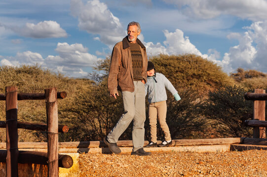 Mature Man and Child Walking Outdoors Near Wooden Fence cloudy sky in the background.