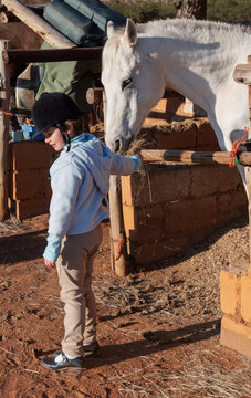 Young Child Feeding White Horse in Rustic Stable Setting with stone walls