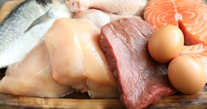 Different types of fresh raw meat, fish and eggs on gray textured table, closeup. Camera zooming in