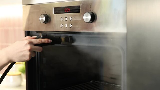 Woman cleaning oven with steam cleaner in kitchen, closeup. Camera moving forward