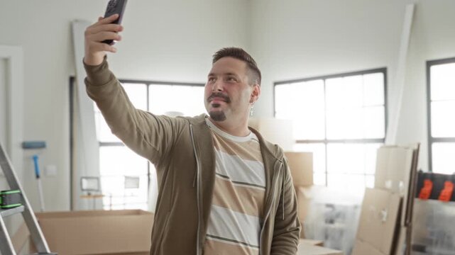 Man raising smartphone for selfie among packed boxes in apartment during move; moving day excitement.