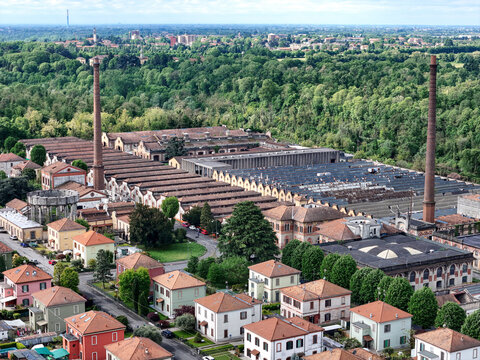 Aerial view of Industrial Village of Crespi d'Adda with historic factory buildings, tall brick chimneys, and residential houses surrounded by green forest Capriate San Gervasio, Lombardia, Italy.