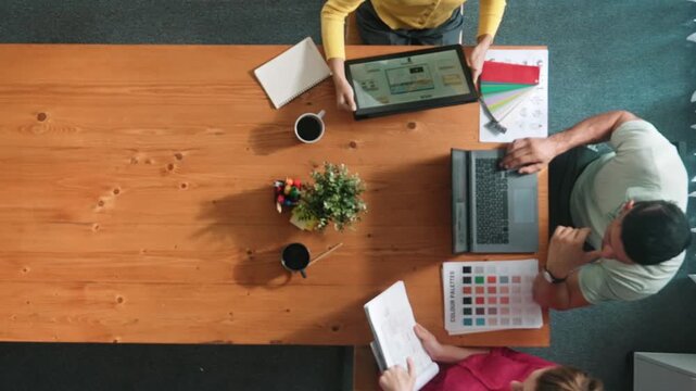 Top aerial view of business people working together to choosing color from color palette. Manager present idea by using tablet to marketing team while business man looking at logo graphic. Symposium.