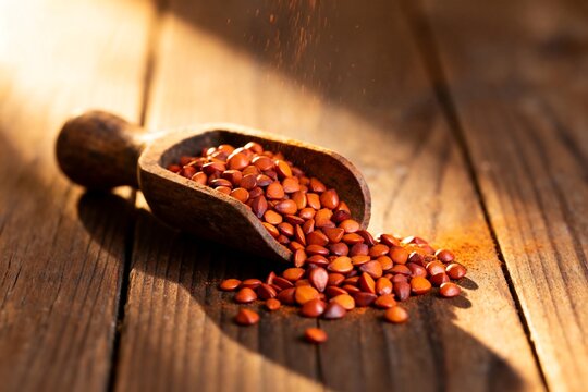 Wooden scoop of annatto seeds on rustic wood surface, warm sunlight