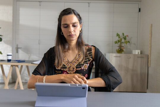 Indian woman sitting at desk using tablet in folio, wearing embroidered tunic and shawl