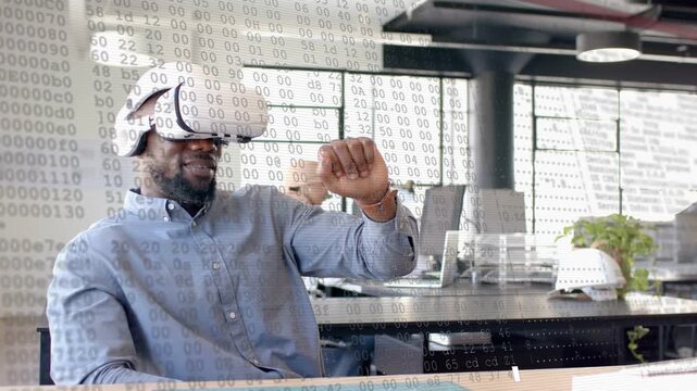 Man wearing VR headset raising hand, manipulating AR overlay, testing tech, coworker on laptop