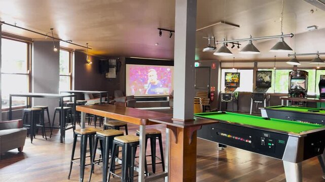 A motion footage showing interior of a modern pub with empty tables, stools, arcade games and pool tables.