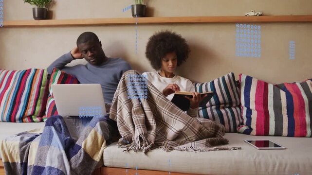 Couple sitting sofa, woman tapping tablet causing HUD graphics rising over laptop fading for tech