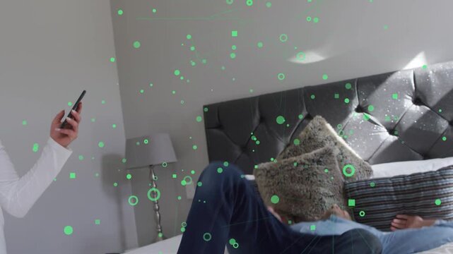 Woman holding phone laughing urging man jumping onto bed while green AR tech overlay circling them