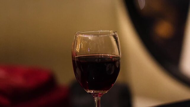 Close up of elegant wine glass filled with red wine against blurry evening city lights background.