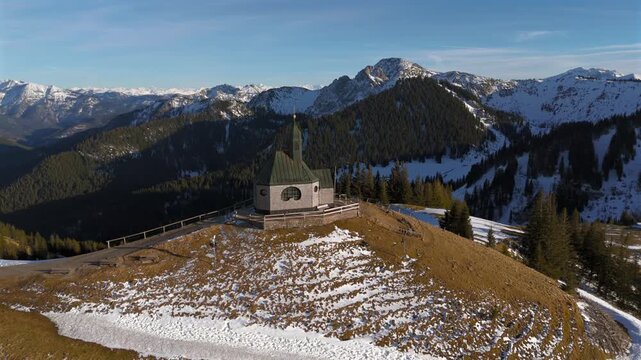 Kapelle Heilig Kreuz Rottach-Egern Tegernsee. Wallbergkapelle on mountain Wallberg overlooking lake Tegernsee and mountain range in sunny spring weather with snow at sunset. Chapel on peak of Alps. 