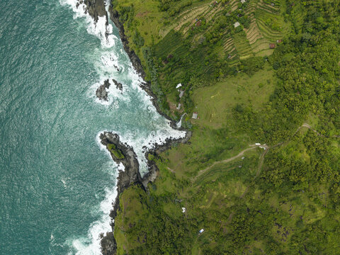Aerial view of Banyutibo Water Fall flowing into the turquoise ocean from lush green terraced cliffs Girisubo, Special Region of Yog, Indonesia.