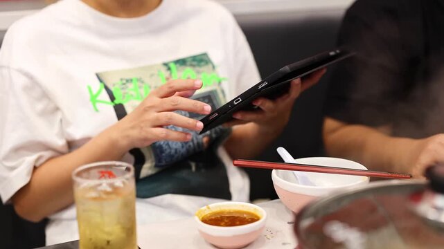 Asian woman using digital tablet to order food at busy japanese restaurant with friends.