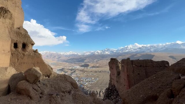 Dramatic timelapse of the Himalayan mountain range and Gangba town viewed through ancient fortress ruins under a blue sky in Tibet China.
