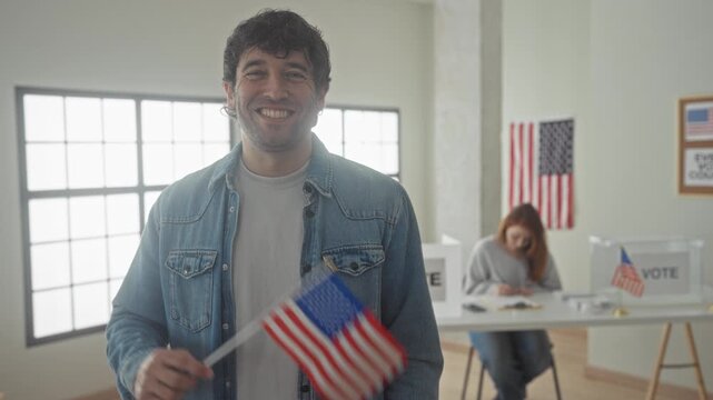 Man waving american flag at polling station building while woman signs ballot at table, flag and vote signs visible; civic duty pride.