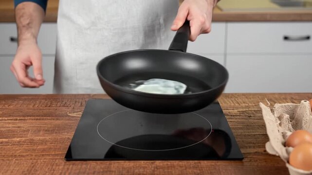 Man cracking a fresh egg into a skillet in kitchen