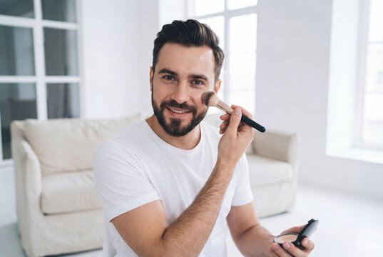 Bearded man applying face bronzer with makeup brush