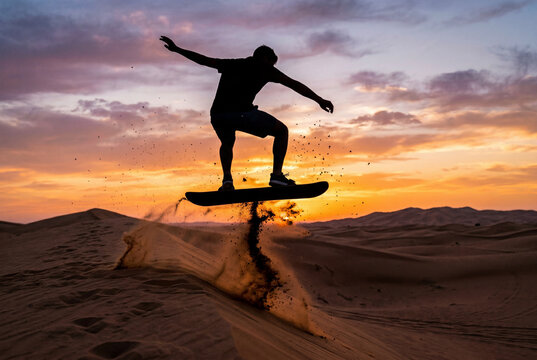 Silhouette of a man jumping on a board over sand dunes at sunset