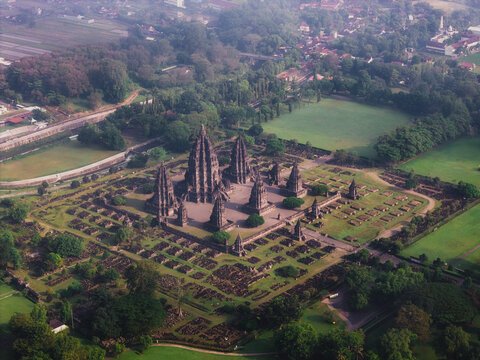 Aerial view of Prambanan Temple with its ancient stone spires, lush green lawns, and surrounding trees under a hazy morning sky Kecamatan Prambanan, Daerah Istimewa Yogya, Indonesia.