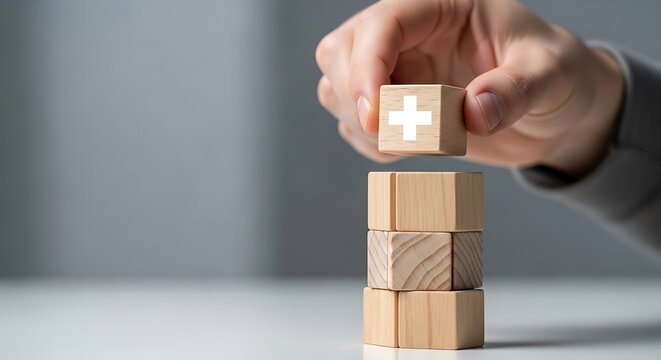 Healthcare symbol on wooden block added to stack by hand. Close-up shot with soft focus and minimalist grey background. Perfect for health insurance and medical benefit commercial brochures.