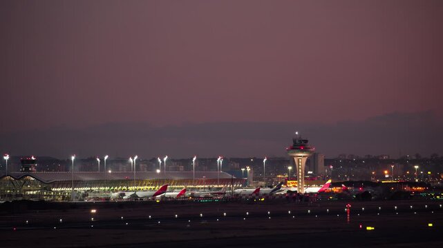 MADRID, SPAIN - MARCH 29, 2026: Wide shot of Madrid Barajas Airport Terminal 4 at dusk. The control tower, terminal building, and tarmac are illuminated. Airplanes are parked at the gates under a