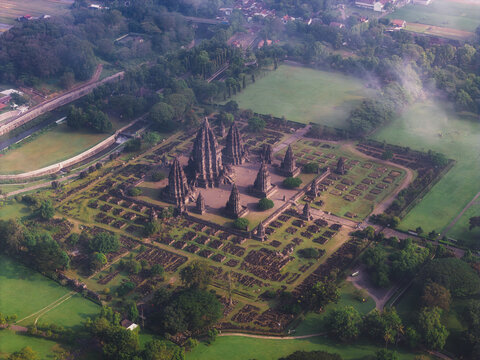 Aerial view of Prambanan Temple, the ancient Hindu temple complex with towering stone structures surrounded by green lawns and morning mist in Kecamatan Prambanan, Daerah Istimewa Yogya, Indonesia.
