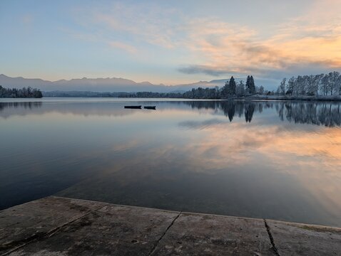 Two small boats moored on a calm Bavarian alpine lake at winter sunset with pastel pink sky reflected in mirror-still water