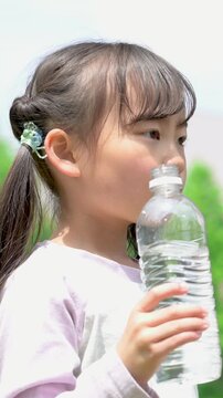 新緑の中熱中症予防など、小学生の子どもの水を飲む水分補給のイメージの縦動画春夏クローズアップ