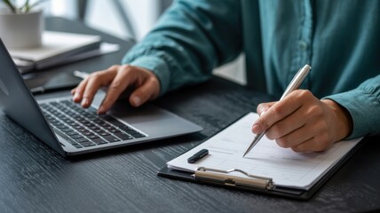Fototapeta premium Persons hands typing on a laptop and writing notes on a clipboard, showcasing efficient multitasking and productivity in a professional setting