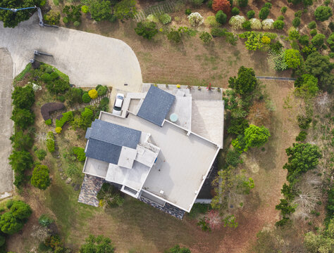 Aerial view of a modern residential house with flat roofs and dark shingles surrounded by lush green trees and a paved driveway in Taiwan.