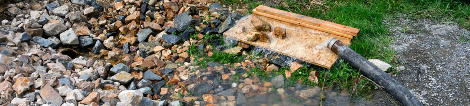 Commercial construction site, heavy duty industrial hose dewatering, pumping excess water out of job site, plywood and rock used to prevent ground erosion before water enters storm drain pipe
