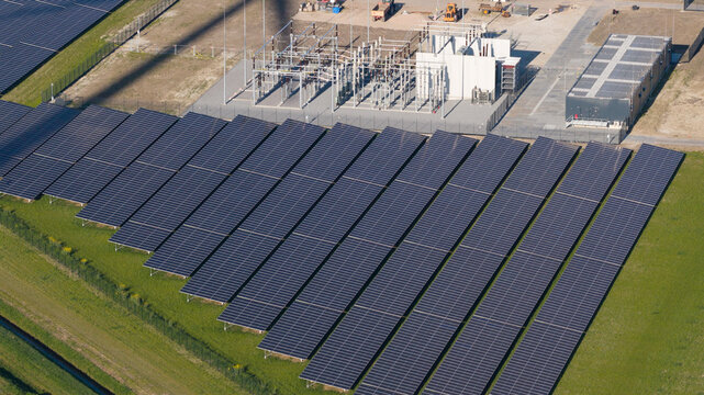 Aerial view of Zonnepark Eekerpolder solar farm featuring rows of photovoltaic panels and an electrical substation on green fields in Scheemda, Groningen, Netherlands.
