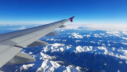 Fototapeta premium Airplane Wing Over Snowy Mountain Range Under Blue Sky.