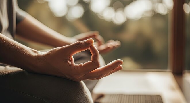Person meditating indoors with hands in gyan mudra position near a window