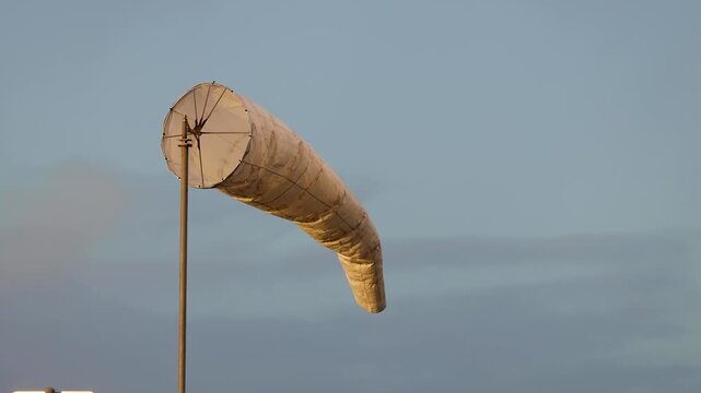 A dirty white windsock against a soft blue sky on a slightly cloudy day in a natural outdoor environment.
