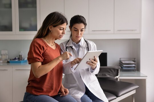 Doctor showing medical information to woman patient on digital tablet, providing lab test results, explaining diagnosis, X-ray imaging, MRI scans, giving medical consultation about treatment options