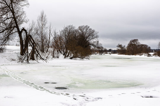 Dangerous thin ice on a snow-covered river with warning footprints. Late winter melt creates hazardous conditions, urging caution