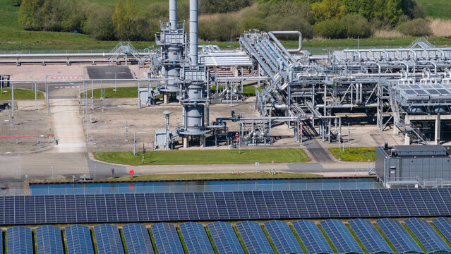Aerial view of the UGS Norg gas storage facility featuring industrial piping, tall exhaust stacks, and a large solar panel array under bright daylight in Langelo, Drenthe, Netherlands.