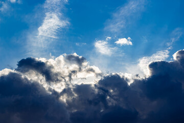 Obraz premium Dramatic sunbeams piercing through heavy dark storm clouds against a vibrant azure sky creating a powerful contrast between light and shadow during a moody afternoon weather event