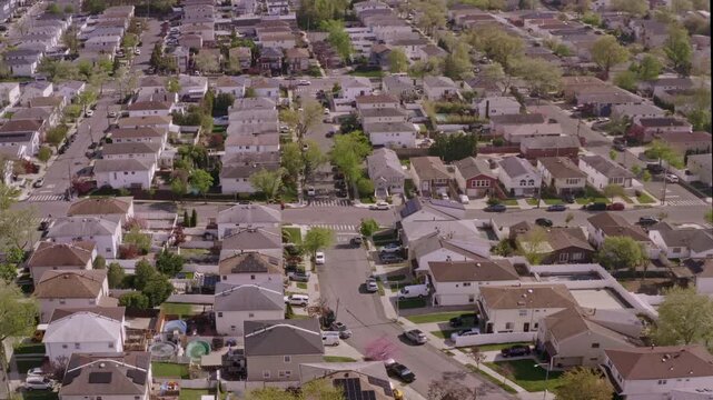 high-angle drone sweep over a quiet residential block, featuring uniform family homes, manicured lawns, and solar panel installations under the soft light of a clear spring day