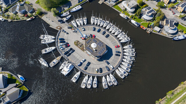 Aerial view of Enjoy Sailing Zeiljachtverhuur with sailboats docked in a circular pattern around a central building and parking area in Lemmer, Friesland, Netherlands.