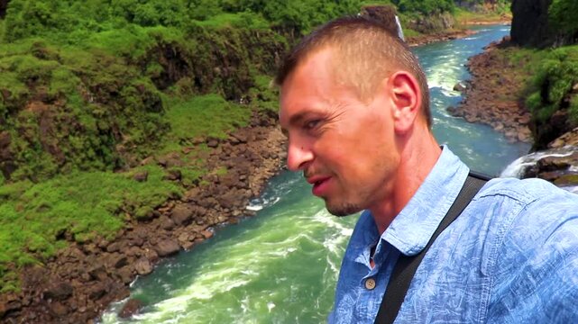 Male traveler photographing Iguazu Falls waterfall tropical rainforest scenic view.