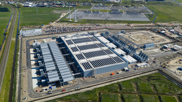 Aerial view of Datacenter Westpoort featuring large industrial buildings with cooling units, a power substation, and surrounding green fields in Groningen, Groningen, Netherlands.