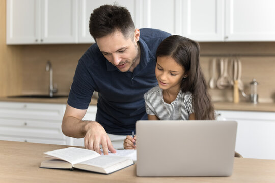 Caring young father helping with school assignment or essay to his little adorable daughter, sit at table in kitchen read textbook, doing tasks or making tests together. Tuition, education, knowledge
