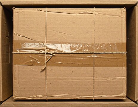 A close-up view of a brown cardboard box secured with tape and twine, nestled inside another cardboard container